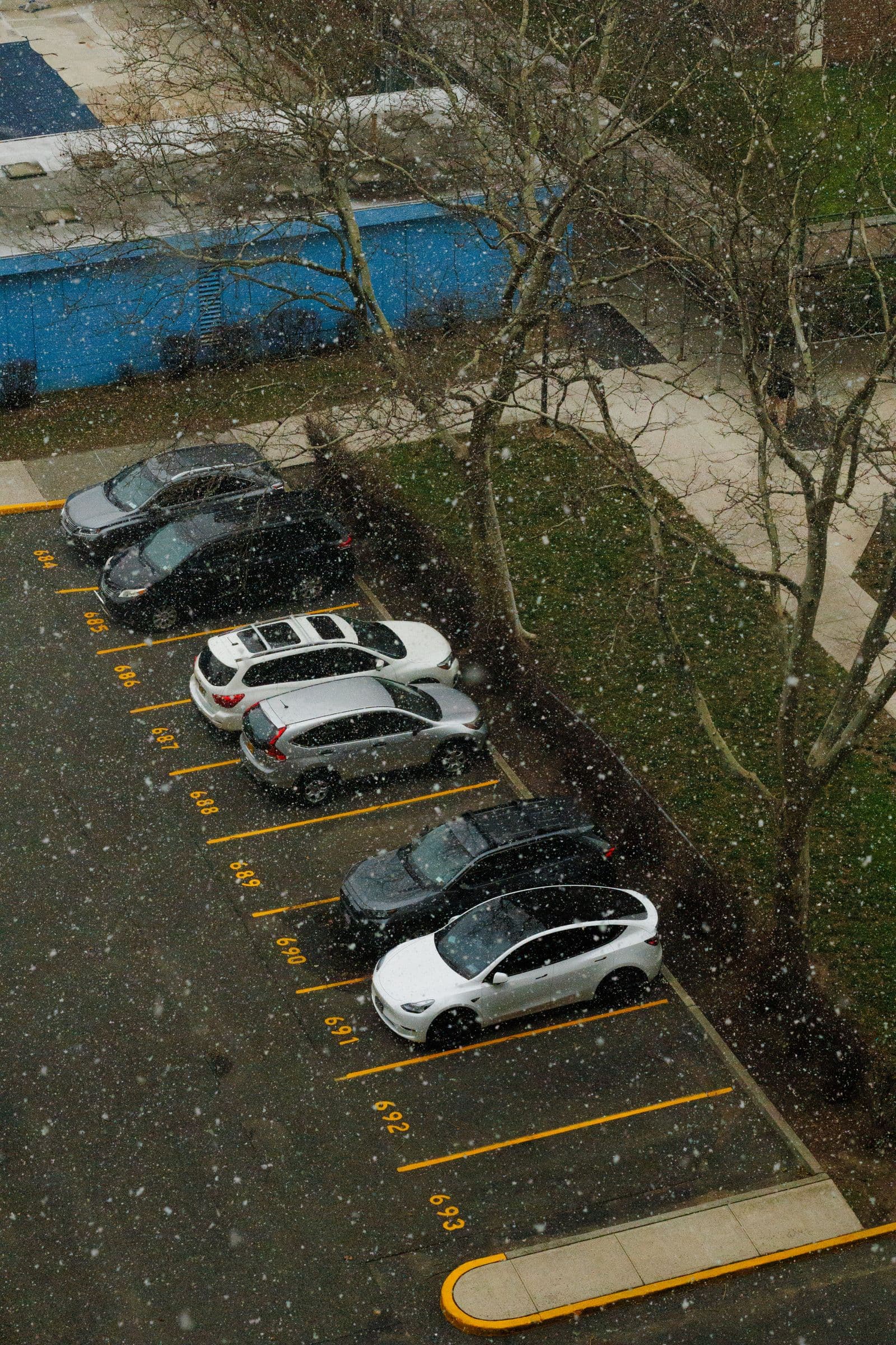 An aerial view of a commercial parking lot covered in snow during light snowfall.