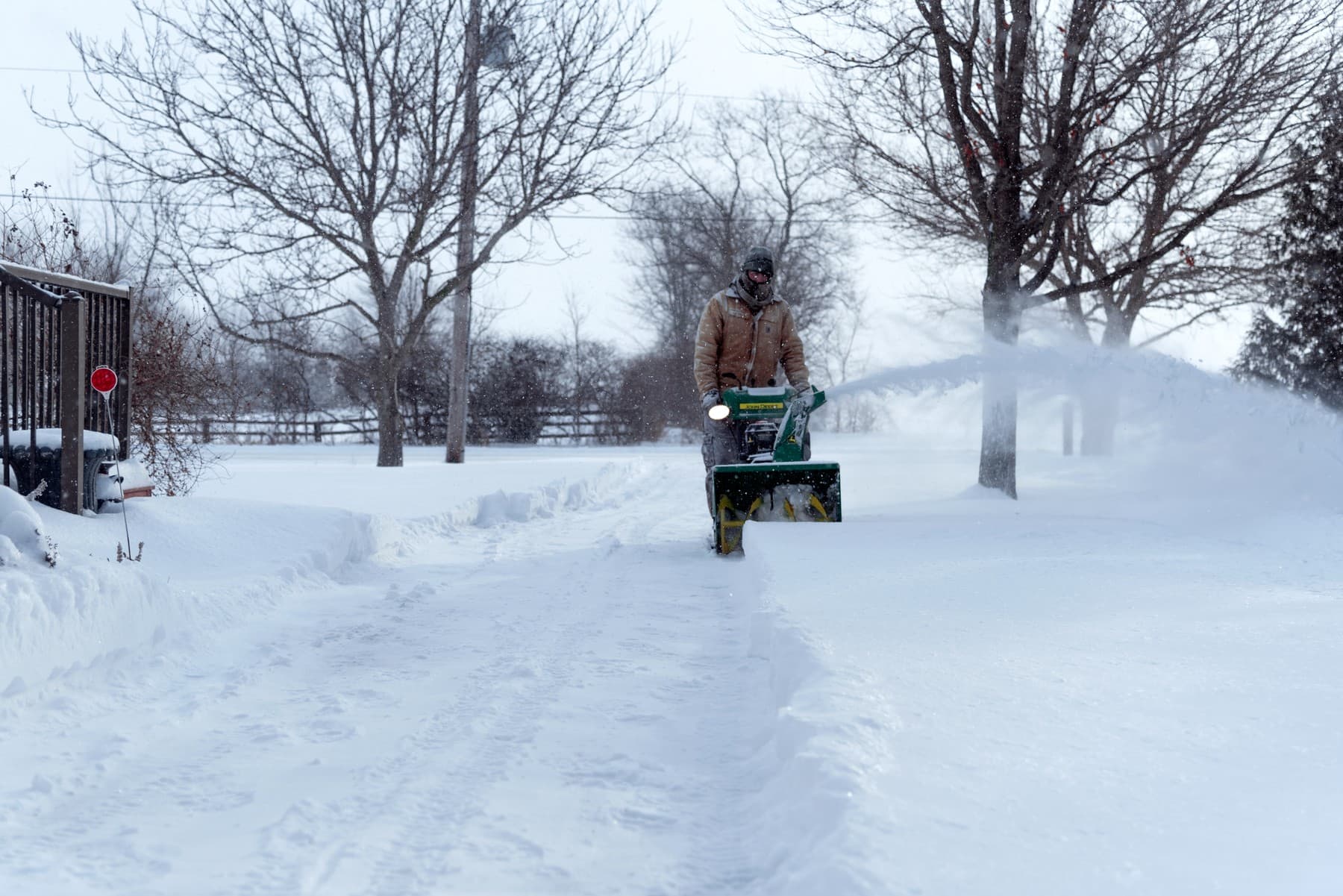 A person clearing a long driveway with a snowblower on a bright winter morning.