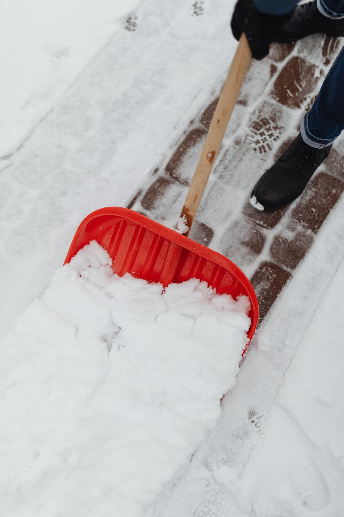 A red shovel clearing snow from a stone walkway.