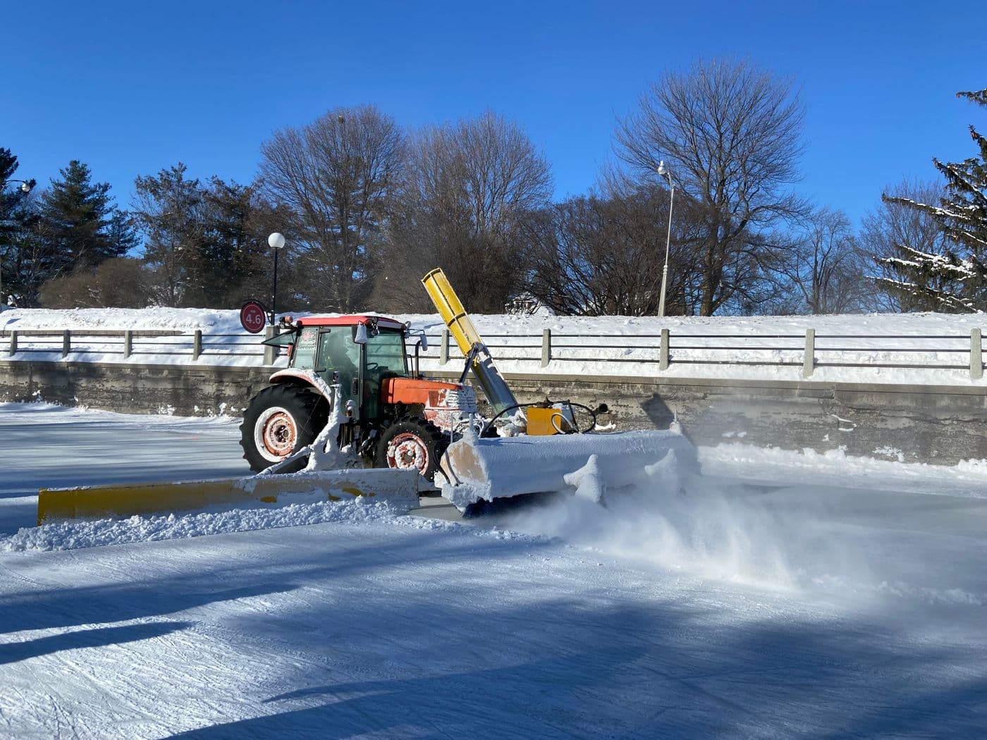A tractor clearing ice off a roadway under a clear blue winter sky.